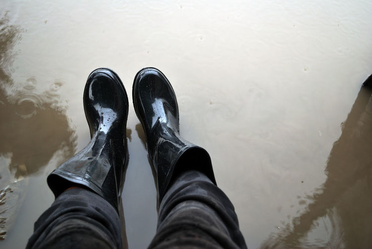 Low section of man wearing rubber boots while standing in puddle