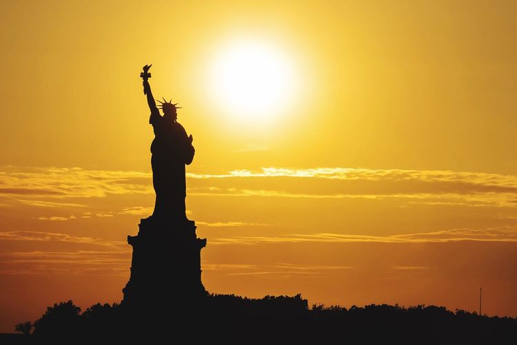 Silhouette statue of liberty against orange sky during sunset