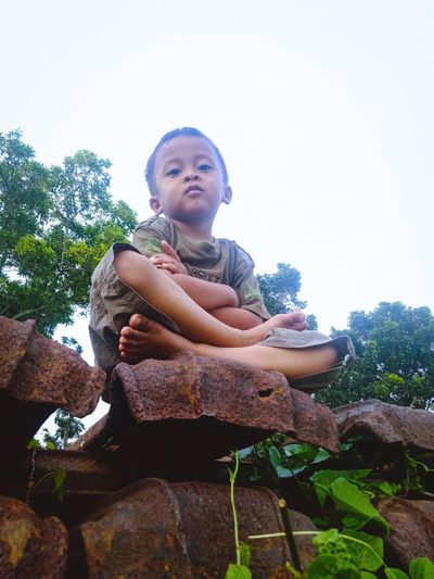 Portrait of girl sitting on rock against sky