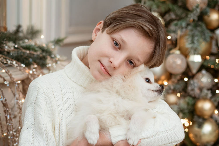 Cute boy with a dog in his arms on the background of a christmas tree