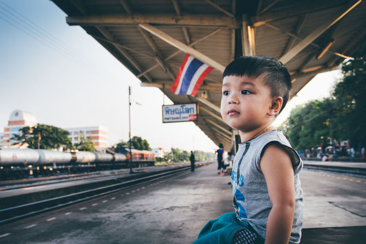 Side view of boy sitting at railroad station platform