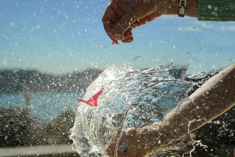 Cropped hands of woman exploding water bomb outdoors