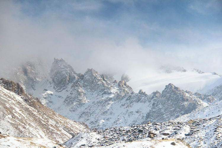 Peaked rocky snow-capped ridge peaks in cloudy fog in tuyuk-su gorge in sunny winter weather