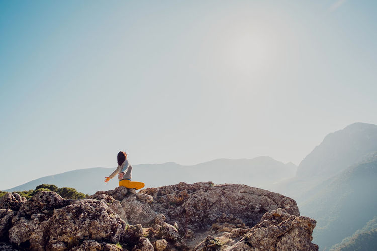 Side view of anonymous female traveler sitting on rock in highlands and doing yoga in padmasana