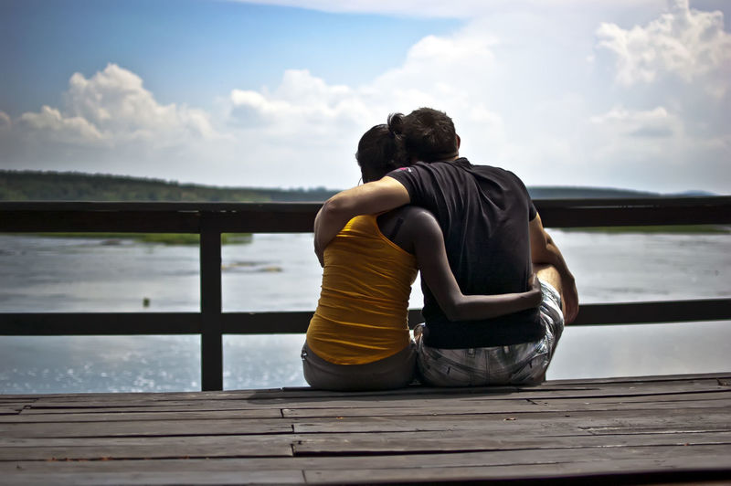 Rear view of couple sitting on pier over sea against sky