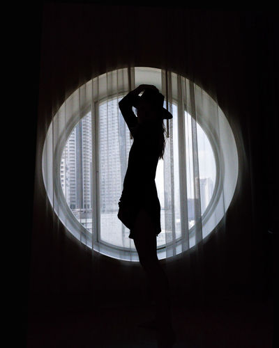 Silhouette woman standing against window