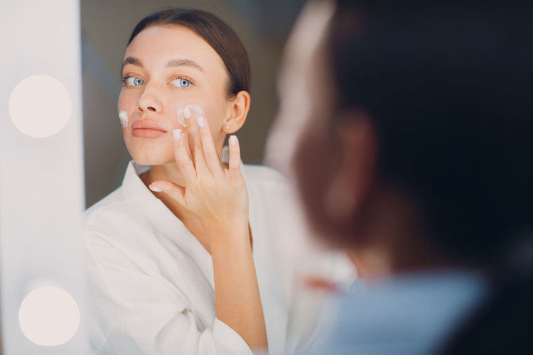 Reflection of woman applying beauty cream
