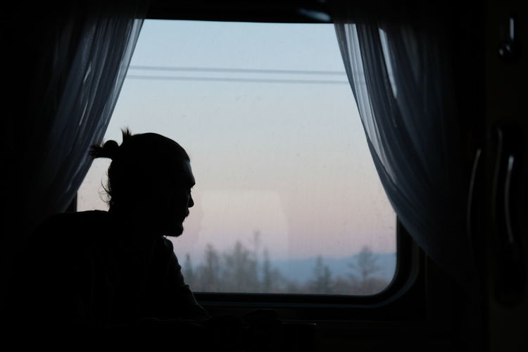 Side view of silhouette man looking through window in train