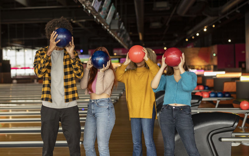 Friends covering face with balls at bowling alley