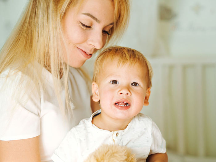 Young beautiful mother with long blond hair having fun with pretty baby boy at home
