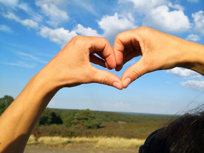 Close-up of hands forming heart shape against sky