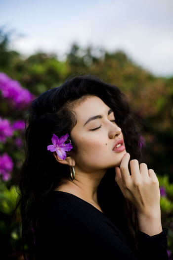 Beautiful young woman with flower sitting against plants