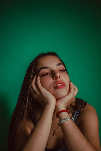 Close-up of thoughtful young woman against green background