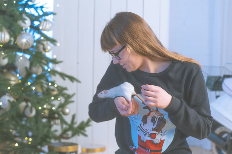 Girl holding rat against christmas tree
