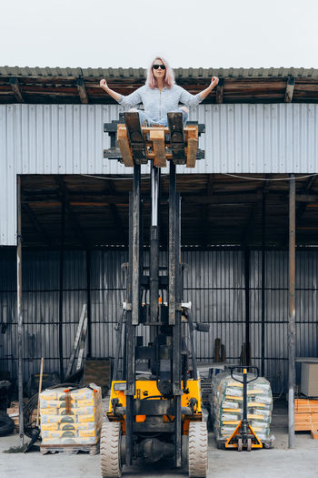 Woman standing on forklift in front of built structure