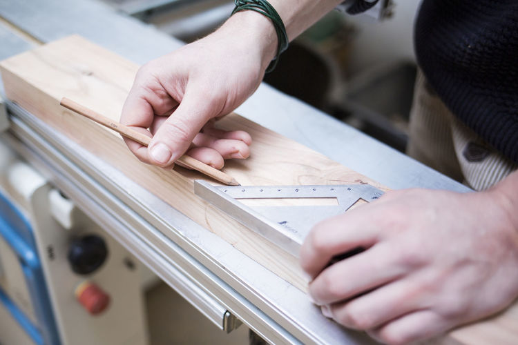 Cropped hands of carpenter measuring wooden planks at workshop