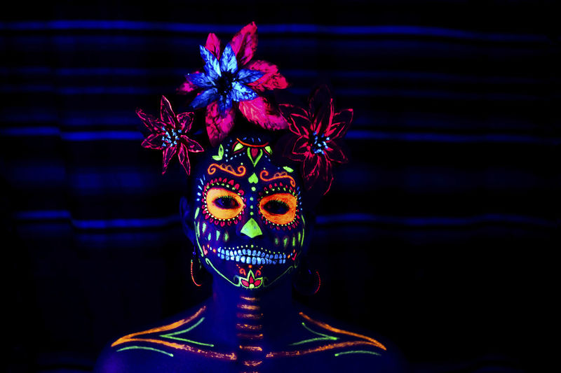Anonymous female in multicolored masquerade mask with flowers on head looking at camera on halloween night