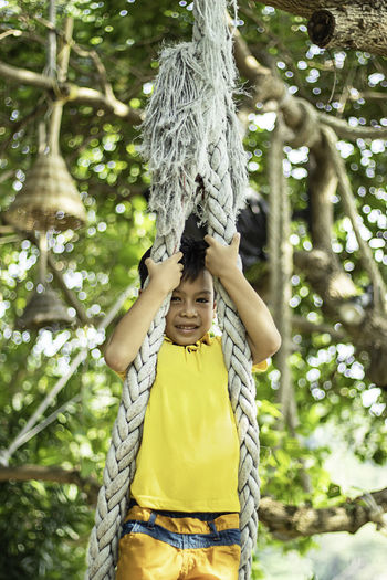Portrait of boy hanging on rope against trees in park