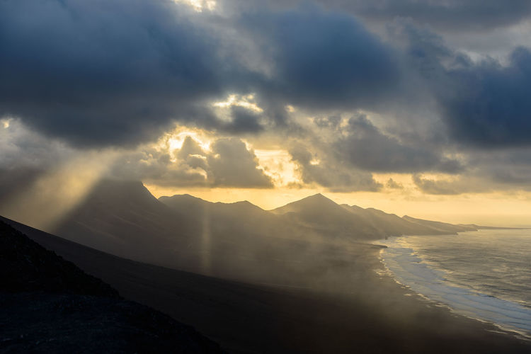 Scenic view of mountains by sea against sky during sunset