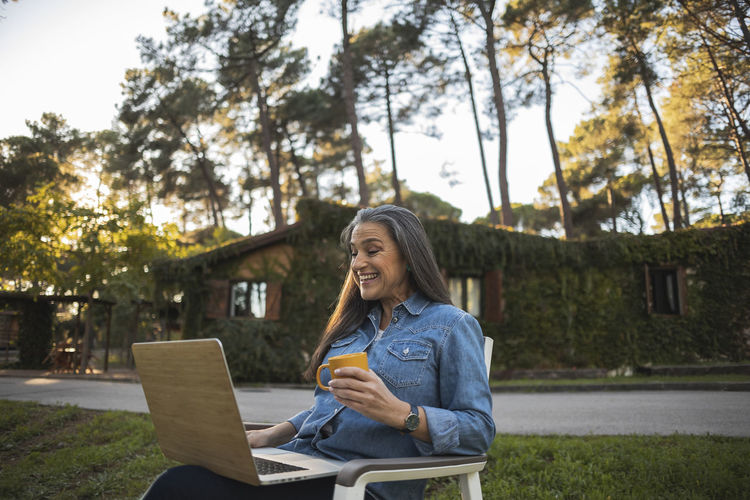 Smiling mature woman sitting outdoors using laptop