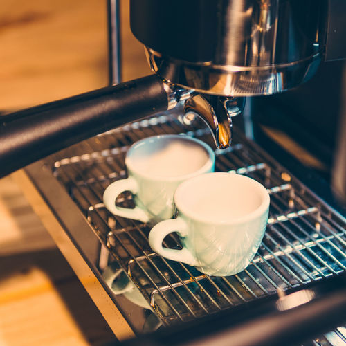 Close-up of drink pouring in cups on espresso maker