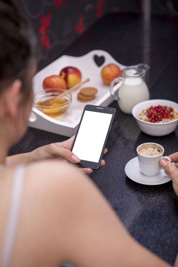 High angle view of woman using smart phone while holding coffee cup on table