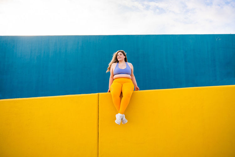 Low angle view of woman sitting against blue wall