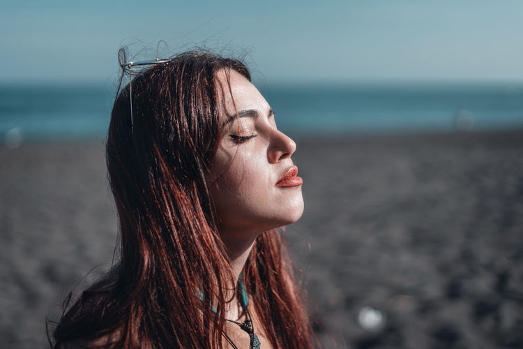 Portrait of young woman at beach against sky