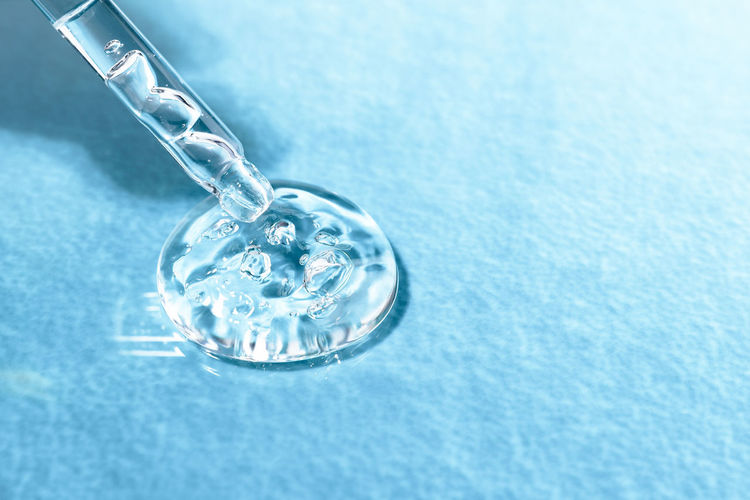 Glass pipette with acid for moisturizing the skin on a blue textural background close-up. 