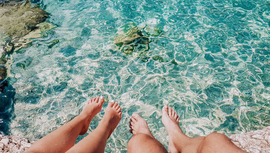 Personal perspective of young couple dangling feet above water on beach.