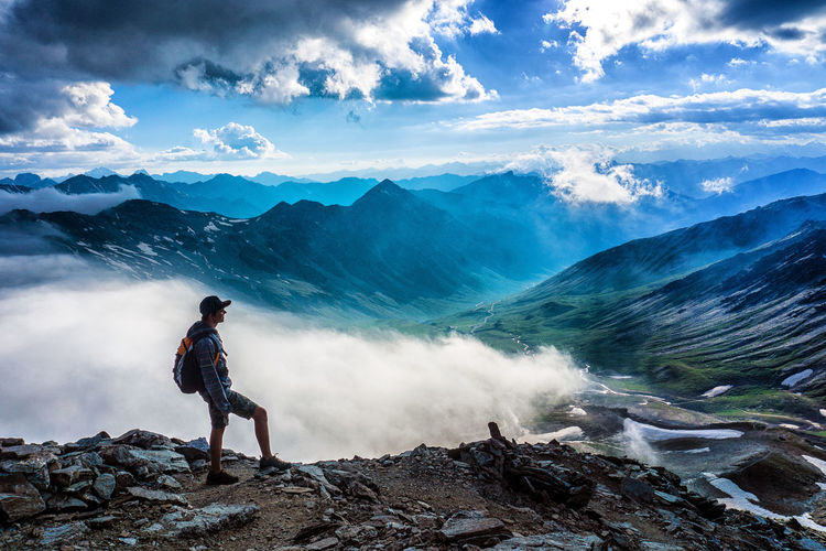 Hiker standing on rocks while looking at mountains against sky
