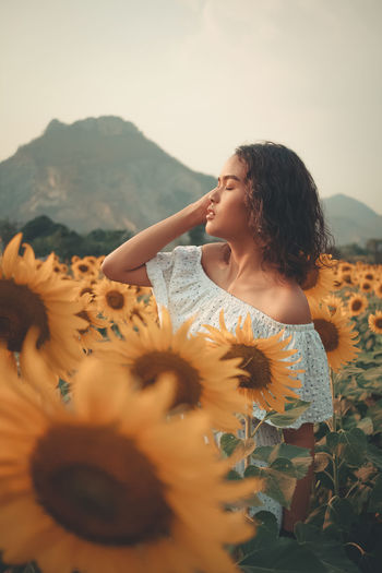 Young woman standing at sunflower farm against sky