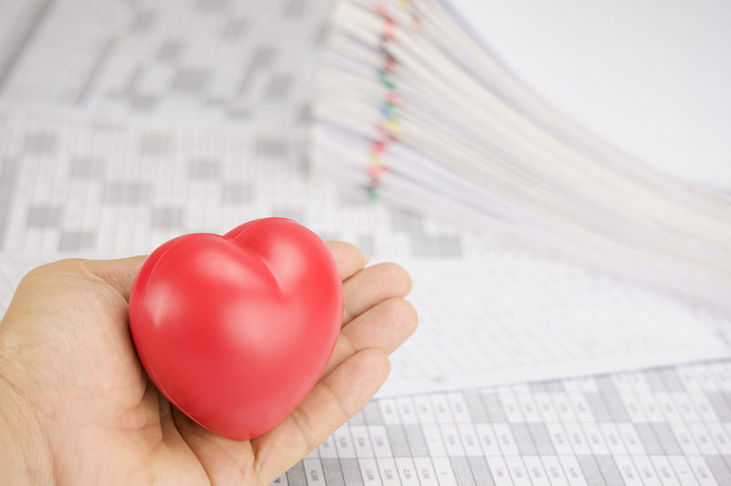 Cropped hand of cardiologist holding heart model by papers