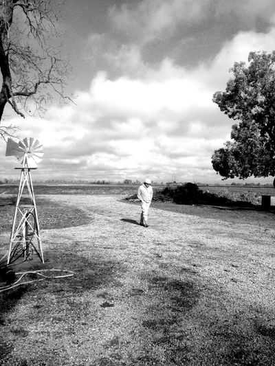 Full length of man walking by water pump windmill on field against sky
