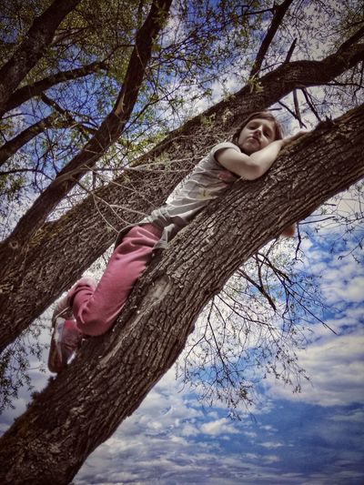 Low angle view of girl sitting on tree against cloudy sky
