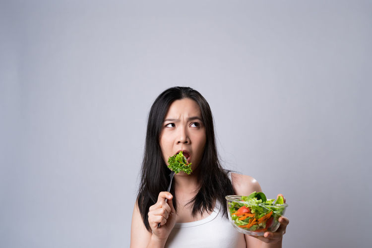 Portrait of woman eating food against white background