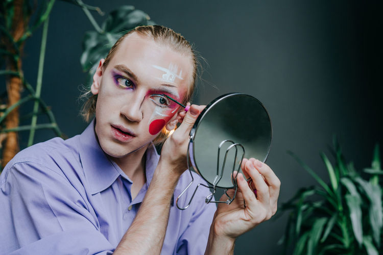 Man applying make-up on face looking in hand mirror