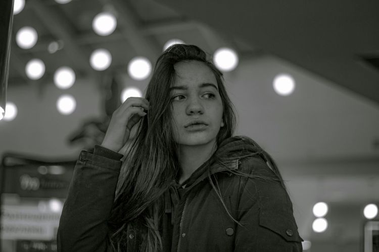 Thoughtful young woman standing against illuminated lights