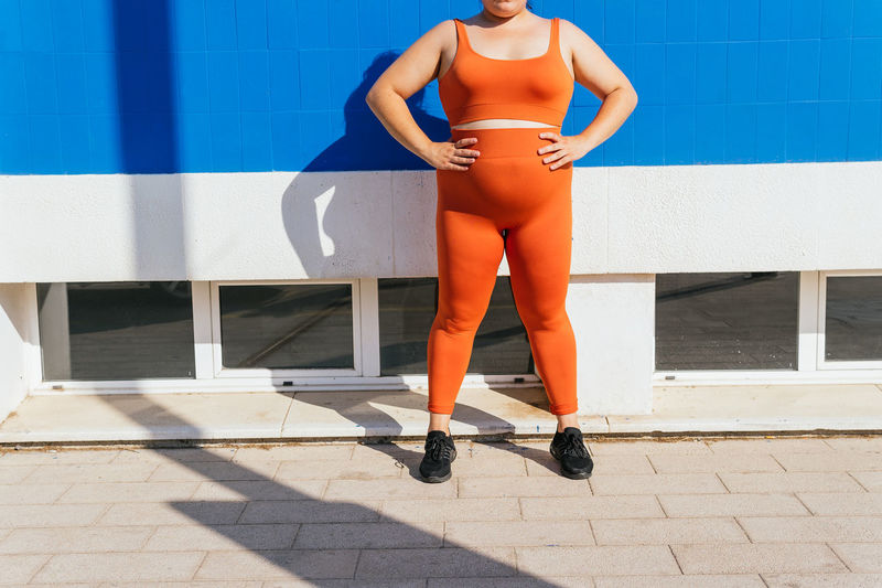 Anonymous overweight ethnic female athlete in active wear against blue tiled wall on sunny day