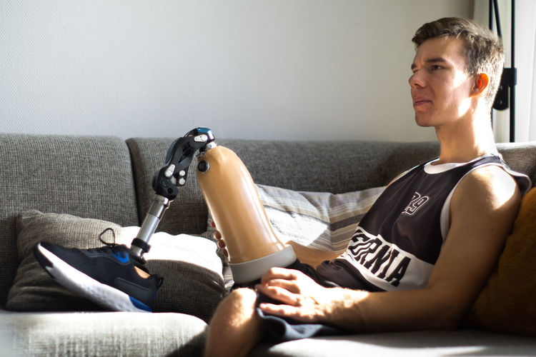 Young man sitting on sofa with prosthetics