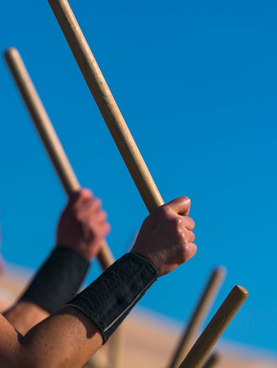 Cropped hands holding stick against clear blue sky