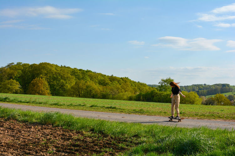 A girl rides a skateboard on a country road in green nature