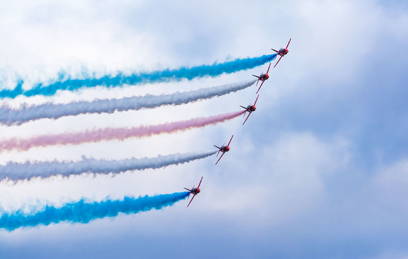 Low angle view of fighter plane performing smoking stunt against cloudy sky