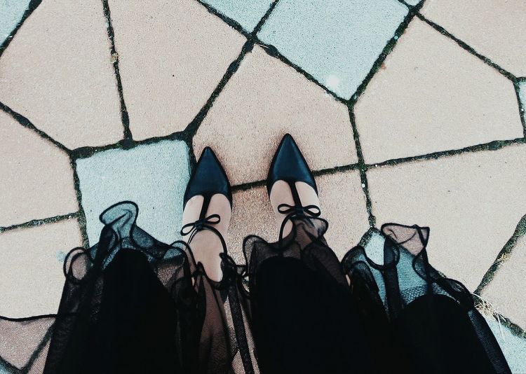 Low section of woman wearing shoes standing on paved footpath
