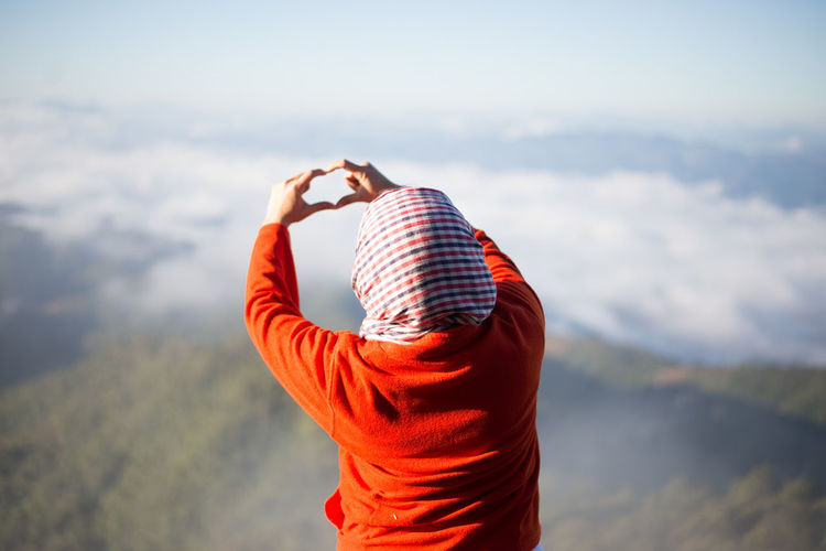 Rear view of woman making heart shape with hands against sky