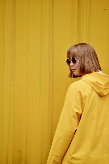 Young woman wearing sunglasses standing against yellow corrugated iron