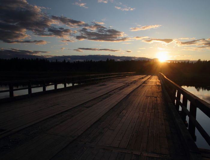 Footpath by lake against sky during sunset