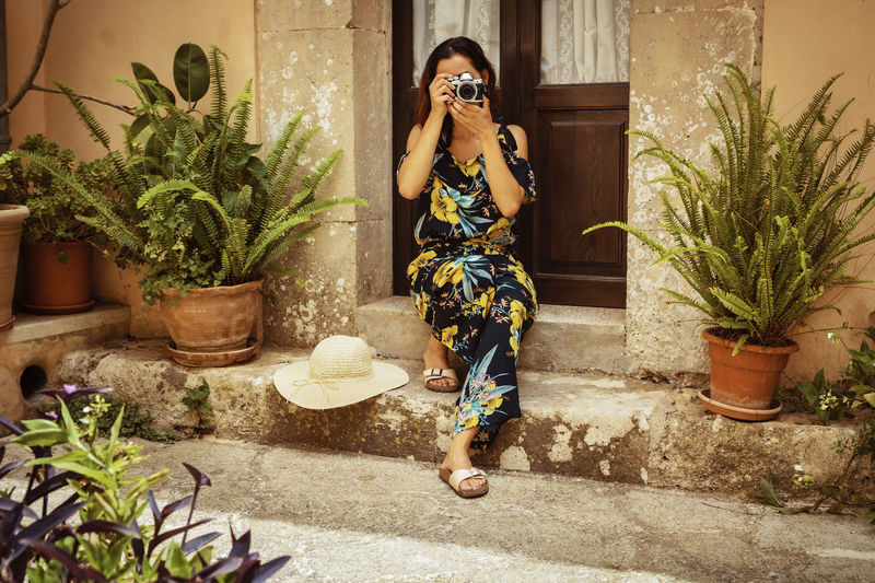 Woman photographing by potted plants outside house