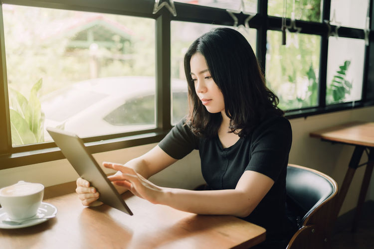 Young woman using phone while sitting on table