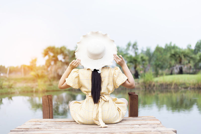 Rear view of woman sitting on pier over lake against sky